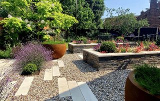 Raised sleeper borders with tiled outer surround blooming and overflowing with flowers and plants of all different shapes, sizes and colours. Border design and landscaped by the Essex Garden Co.