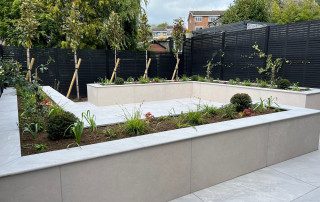 Raised sleeper beds, made of light grey porcelain tiles in paved garden. Before image showing borders at the early stages of growth. Designed and landscaped by the Essex Garden Co.
