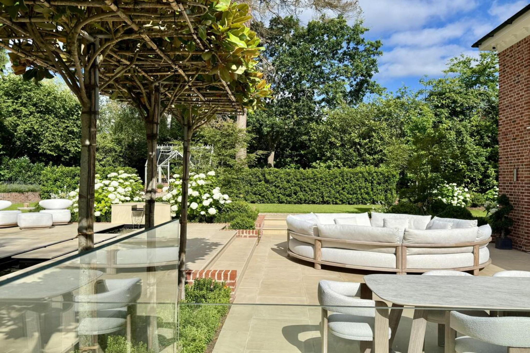 Fryerning, Essex garden transformation. Expansive front and back garden renovation. New build plot, featuring: sandstone paving, brickwork, fire-pit, lighting, planting, irrigation, glass house, water rill, and umbrella trees. Garden design and professional landscaping by The Essex Garden Co.