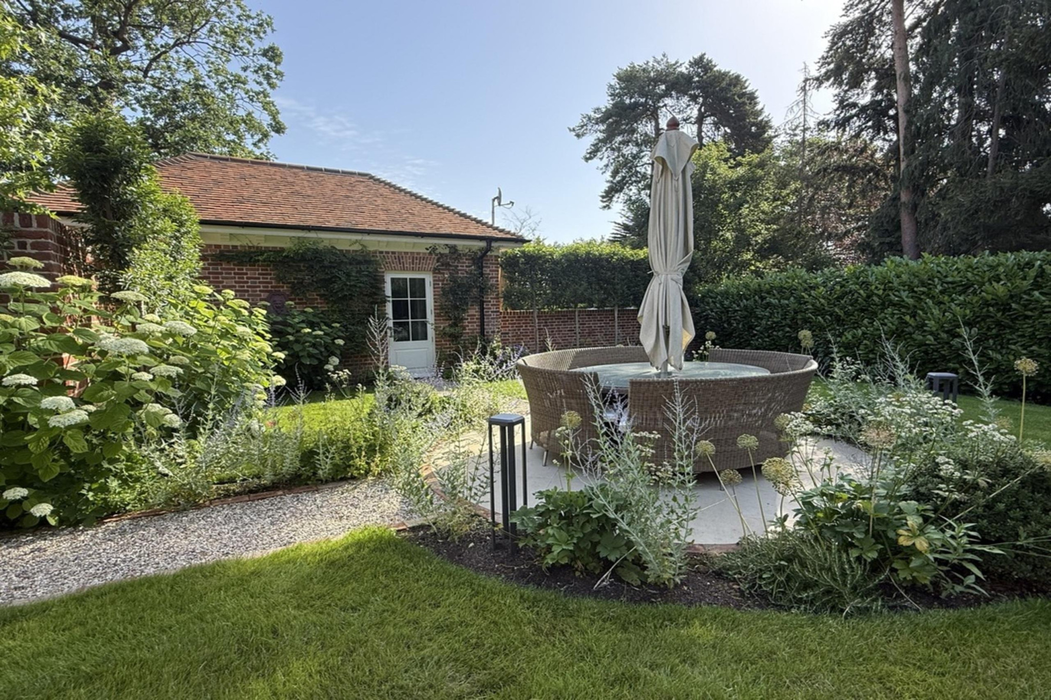 Fryerning, Essex garden transformation. Expansive front and back garden renovation. New build plot, featuring: sandstone paving, brickwork, fire-pit, lighting, planting, irrigation, glass house, water rill, and umbrella trees. Garden design and professional landscaping by The Essex Garden Co.