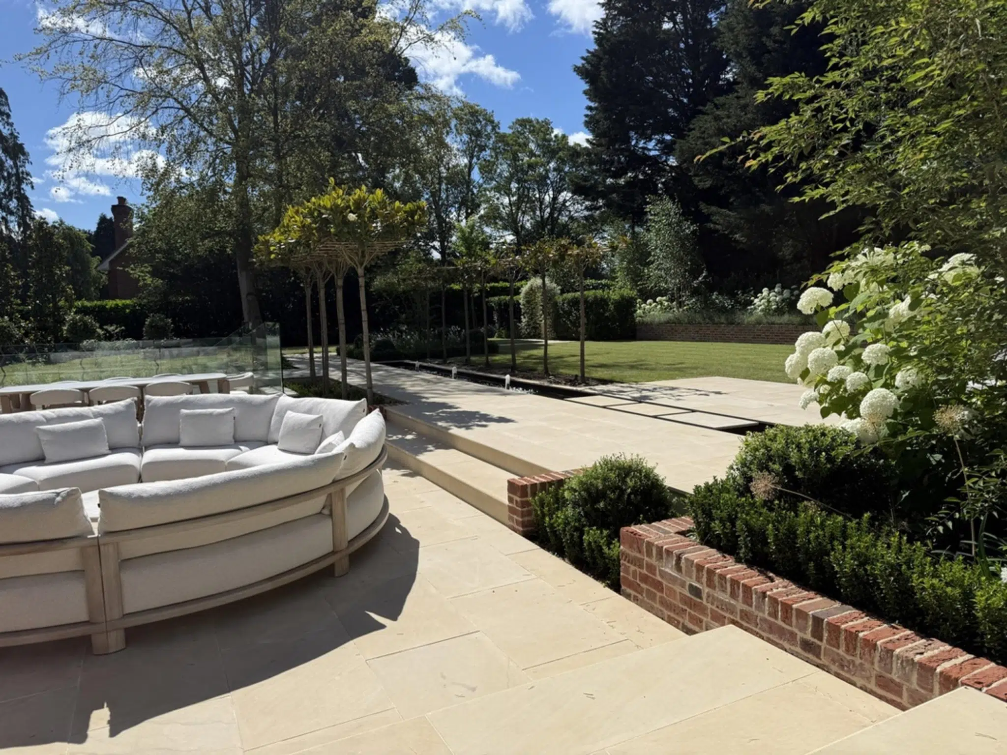 Fryerning, Essex garden transformation. Expansive front and back garden renovation. New build plot, featuring: sandstone paving, brickwork, fire-pit, lighting, planting, irrigation, glass house, water rill, and umbrella trees. Garden design and professional landscaping by The Essex Garden Co.