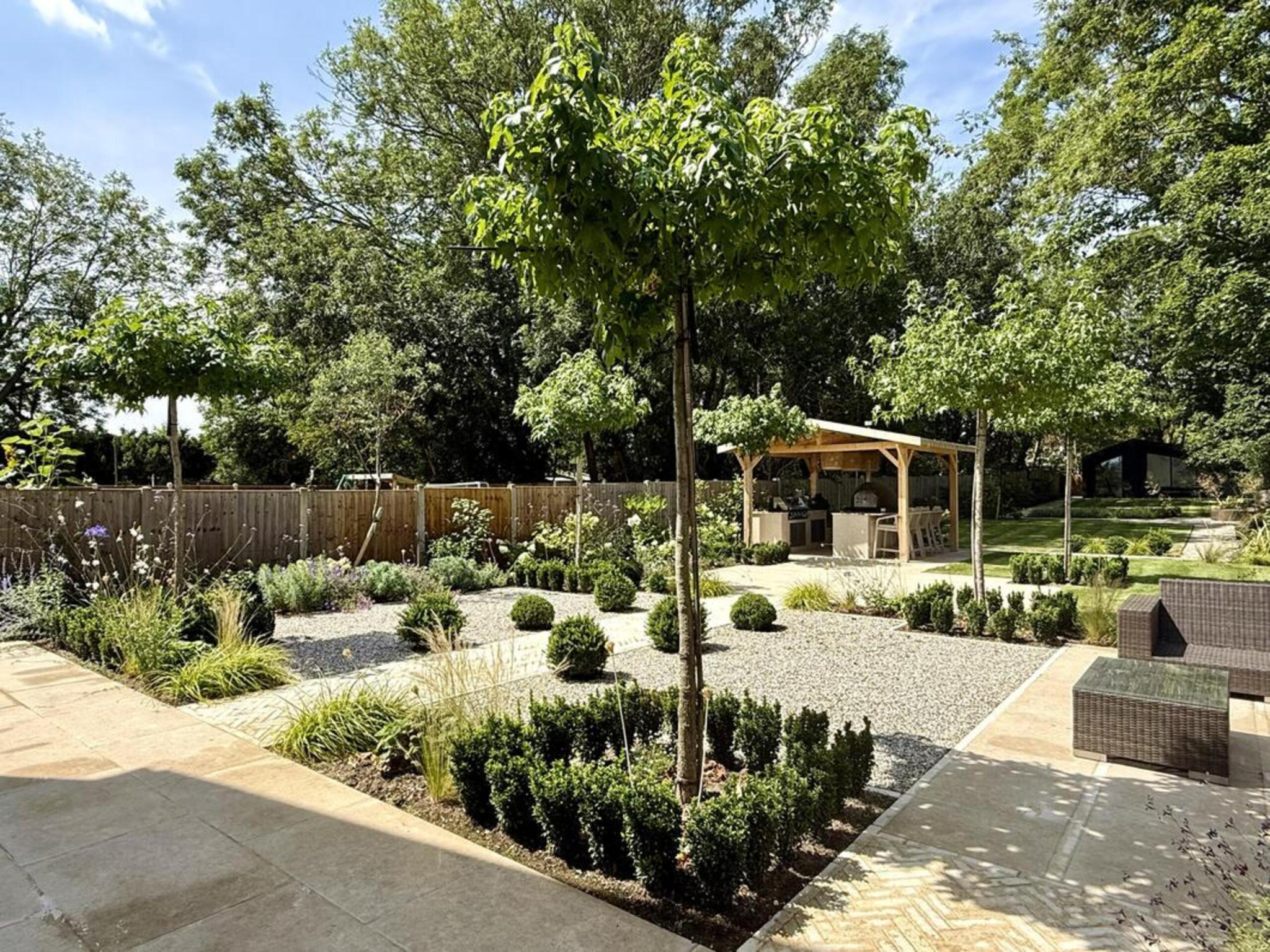 Garden transformation in Hall Lane, Upminster. Essex garden design and landscaping features: porcelain paving, feature pavers, timber gazebo, outdoor kitchen, umbrella trees, lighting, planting, turf, stabilising grids, gravel and irrigation.