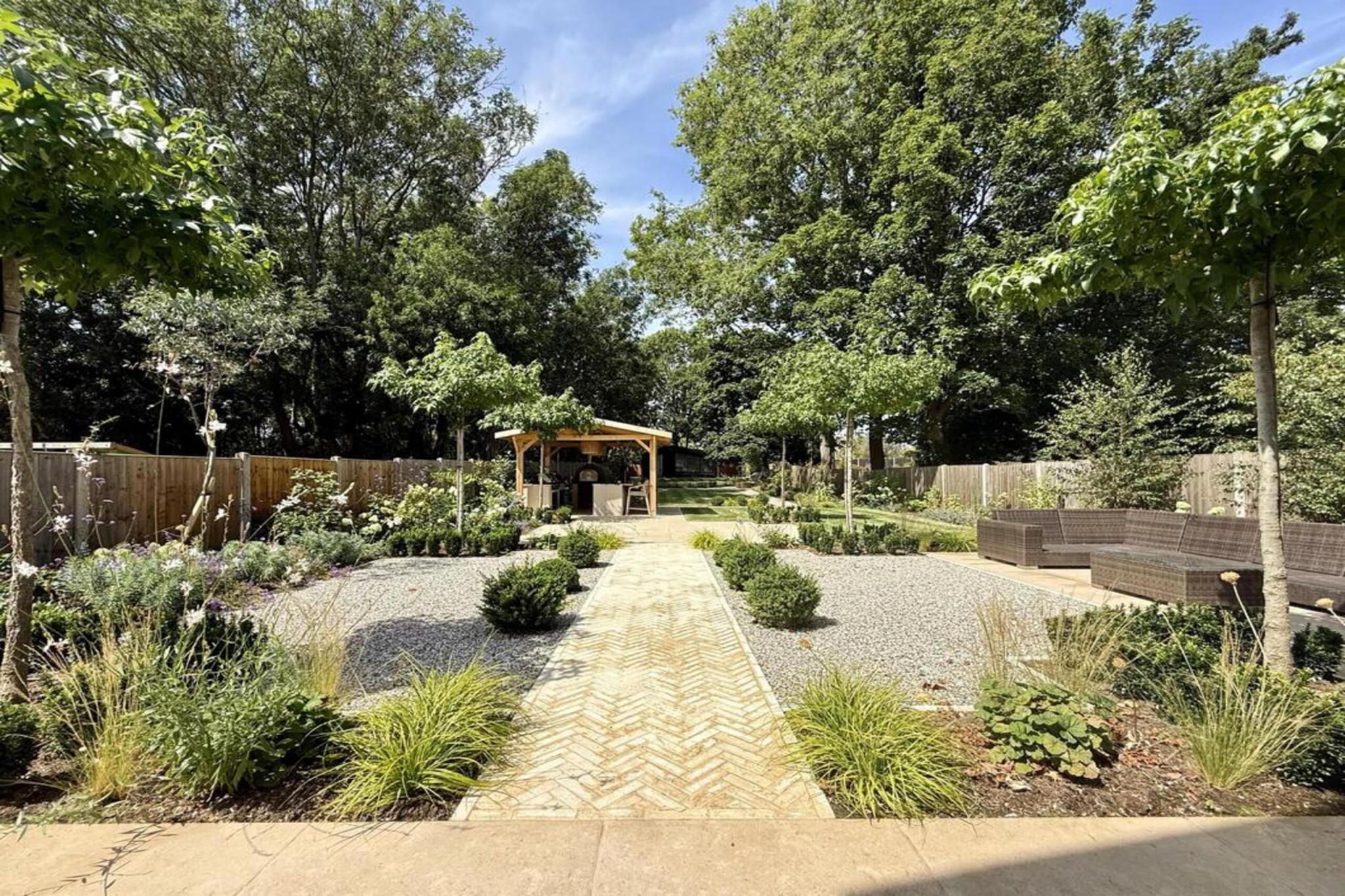 Garden transformation in Hall Lane, Upminster. Essex garden design and landscaping features: porcelain paving, feature pavers, timber gazebo, outdoor kitchen, umbrella trees, lighting, planting, turf, stabilising grids, gravel and irrigation.