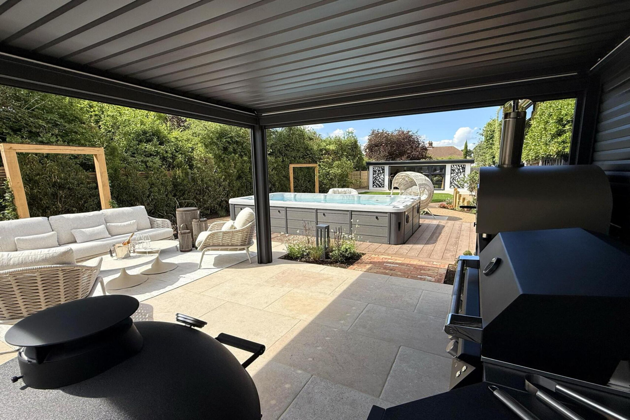 Garden transformation in Corbetts Avenue, Upminster. Essex. Features include: porcelain paving, clay pavers, louvered pergola, outdoor kitchen, swim spa, rain arch, lighting, planting, turf, resin, Irrigation. Garden design and lanscape transformation by The Essex Garden Co.